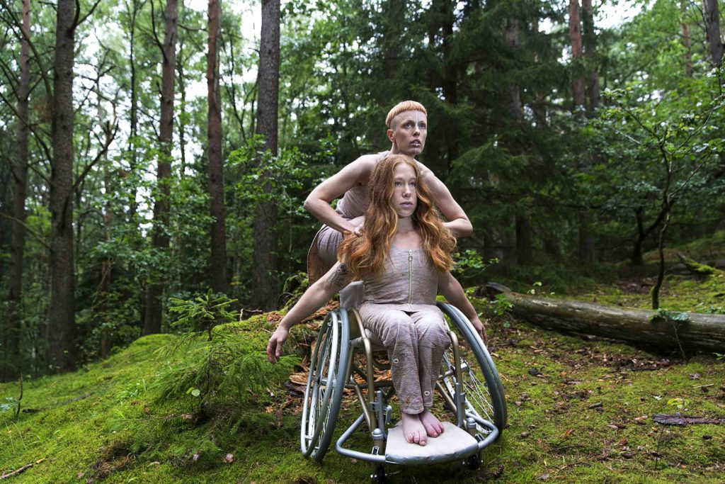 Två dansare i skogen. Den ena i rullstol den andra står bakom.